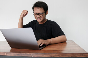 Happy excited Asian man with laptop and raising his arm up to celebrate success or achievement.