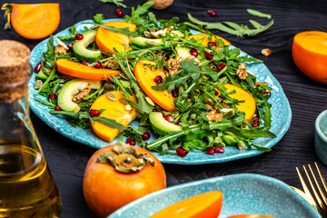 Gourmet salad with persimmon, avocado, pumpkin seeds, walnuts, pomegranate and arugula on a light...
