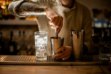 male bartender prepares cocktail in shaker cup using the muddler