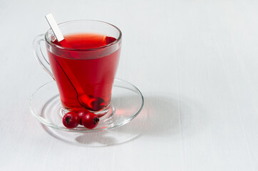 Red tea in elegant transparent cup with ripe hawthorn berries in sunlight on white wood board, copy space.