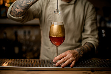 bartender holds piece of ice over glass with fizzy drink decorated with gold