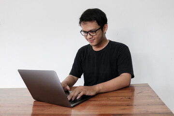 Young Asian man is serious work or thinking in the front the laptop. Indonesia Man wear black shirt Isolated grey background.