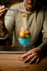 man holds slice of citrus over wine glass decorated with gold