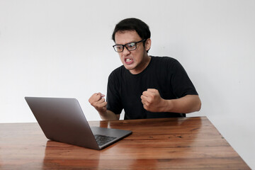 Young Asian man is Angry and hate with laptop. Indonesia Man wear black shirt Isolated grey background.