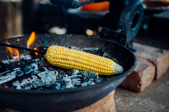 A tender corncob is roasted on a fire in road side food stall in India. A popular roadside food during rainy season.
