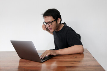 Young Asian man is Angry and hate with laptop. Indonesia Man wear black shirt Isolated grey background.