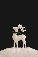 White reindeer with green christmas garland standing in the snow with a black background. New Year minimal concept