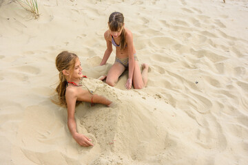 Girl bury her girlfriend with sand on the sandy beach