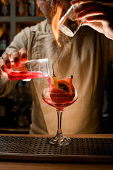 barman masterfully add ingredients to glass with vegetables inside and makes fire over it