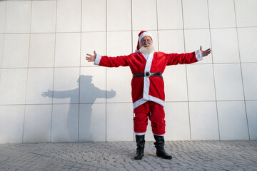 Santa Claus on the street, standing against a gray modern wall. White beard, a red suit with a hat. Christmas, New year. grandfather Frost. Grey modern background, copy spaces