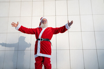 Santa Claus on the street, standing against a gray modern wall. White beard, a red suit with a hat. Christmas, New year. grandfather Frost. Grey modern background, copy spaces