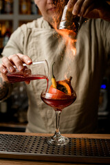 bartender add ingredients to glass with small pumpkin inside and makes fire over it