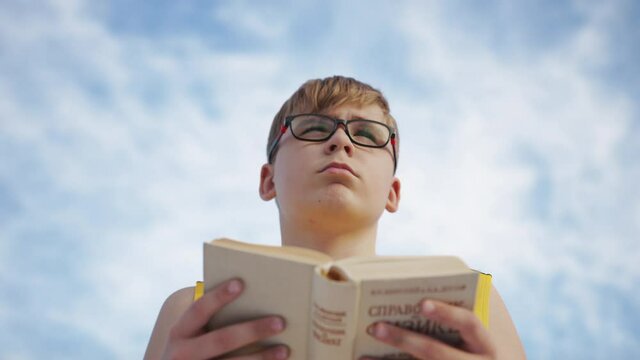 Young boy reading a book on a background of the sky