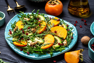 Fresh fruit salad with persimmons, arugula, avocado, pumpkin seeds, walnuts, pomegranate on a wooden background, Diet menu. Vegan food