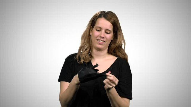 Woman demonstrates wearing black surgical gloves, medium shot over white background.