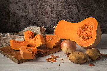 Selective focus shot of Butternut squash sliced on a cutting board with onion and potatoes