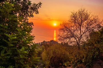 scenic view at picturesque sunset from high mountain with bushes and green trees below and beautiful cloudy sky, sea with far coast, sun glow with reflection on the background , castle landscape