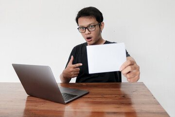 Wow face of Your Asian man shocked and surprised with laptop and holding empty white space paper.
