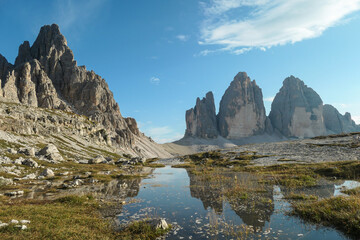 Obraz premium A panoramic view on the famous Tre Cime di Lavaredo (Drei Zinnen), mountains in Italian Dolomites. The mountains are reflecting in small paddle. Desolated and raw landscape. Natural phenomenon