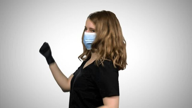 Woman with a surgical mask and gloves dancing and celebrating, extremely happy, over white background.