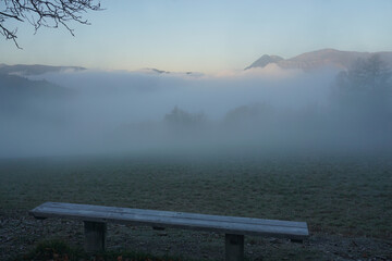 misty fog lifting on the mountains of the French Alps with a frozen bench