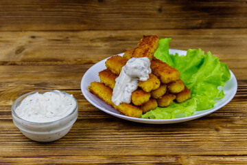 Fried fish fingers on a plate with lettuce and tartar sauce on wooden table