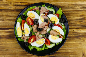 Tasty tuna salad with lettuce, black olives, eggs and fresh vegetables on wooden table. Top view