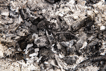 Gray natural black ash pile grunge abstract texture background. Charcoal after burning on a bonfire, pieces of burnt paper plastic bottles or wood branches bark of tree. Image with copy empty space