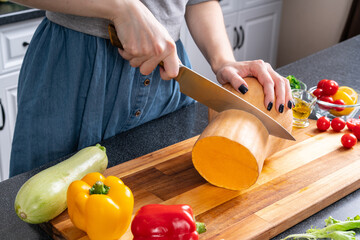 Preparing for home party. Woman cuts pumpkin on cutting board.