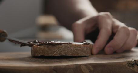 man spreading chocolate hazelnut spread on ciabatta slice on wood board
