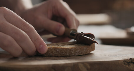 Fototapeta na wymiar man spreading chocolate hazelnut spread on ciabatta slice on wood board