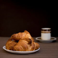 Croissants on a plate and a cup of coffee on a dark background