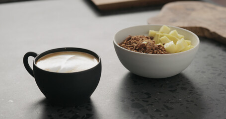 cappuccino in black cup with granola with mango in white bowl on kitchen