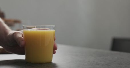man hand take orange juice in thin glass from countertop