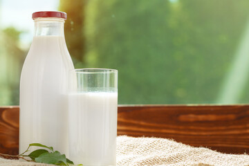 Bottle and glass of milk on wooden table against blurred foliage background
