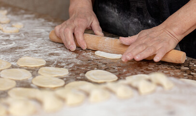 Woman rolls the dough with a rolling pin on the table.
