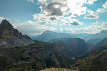 A panoramic view on a vast valley in Italian Dolomites. The valley is surrounded with high mountains from each side. There are a few clouds above. Remote and isolated place. Remedy