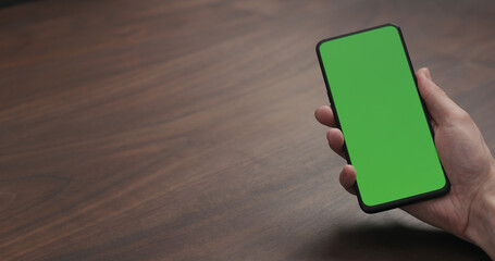 man hold smartphone with greenscreen on walnut table