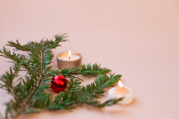 Christmas composition. Fir branch with Christmas tree decorations and candles on a pink background. Selective focus