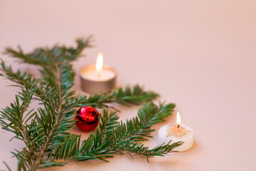 Christmas composition. Fir branch with Christmas tree decorations and candles on a pink background. Selective focus