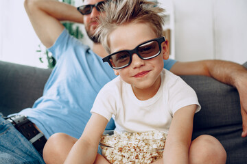 Obraz premium Father and son watching movies at home in 3d glasses and eating popcorn