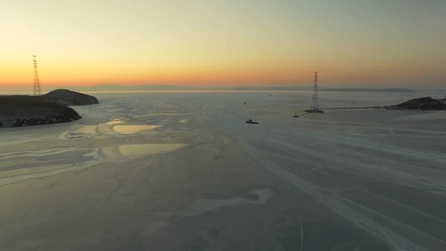 Drone view of the ice-bound strait with tugboats operating at sunset