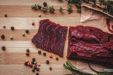 Close-up of basturma sliced into pieces. Dried meat with spices cut into slices. Dried horse meat on a wooden board with rosemary and caraway herbs