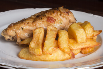 Close-up of French fries on a ceramic plate with chicken and vegetables in the background. Food presentation.