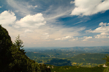Letni krajobraz górki,  widok na zielone pola i lasy pod niebieskim niebem z chmurami