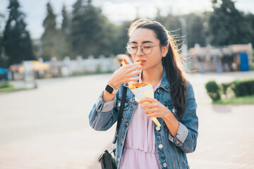 Asian girl eating street food French fries in paper bag
