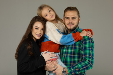 Portrait of attractive father, daughter and mother embracing together in front of grey background.