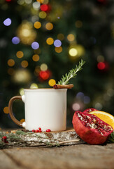 Blank white ceramic cup in festive arrangement with Christmas tree bokeh light in the background.
