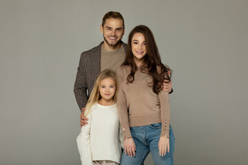 Portrait of attractive father, daughter and mother embracing together in front of grey background.