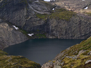 Stunning view of Fjerddalsvatnet lake surrounded by steep mountains with tall waterfall on Moskenesøy island, Lofoten, Norway with snow and green vegetation.